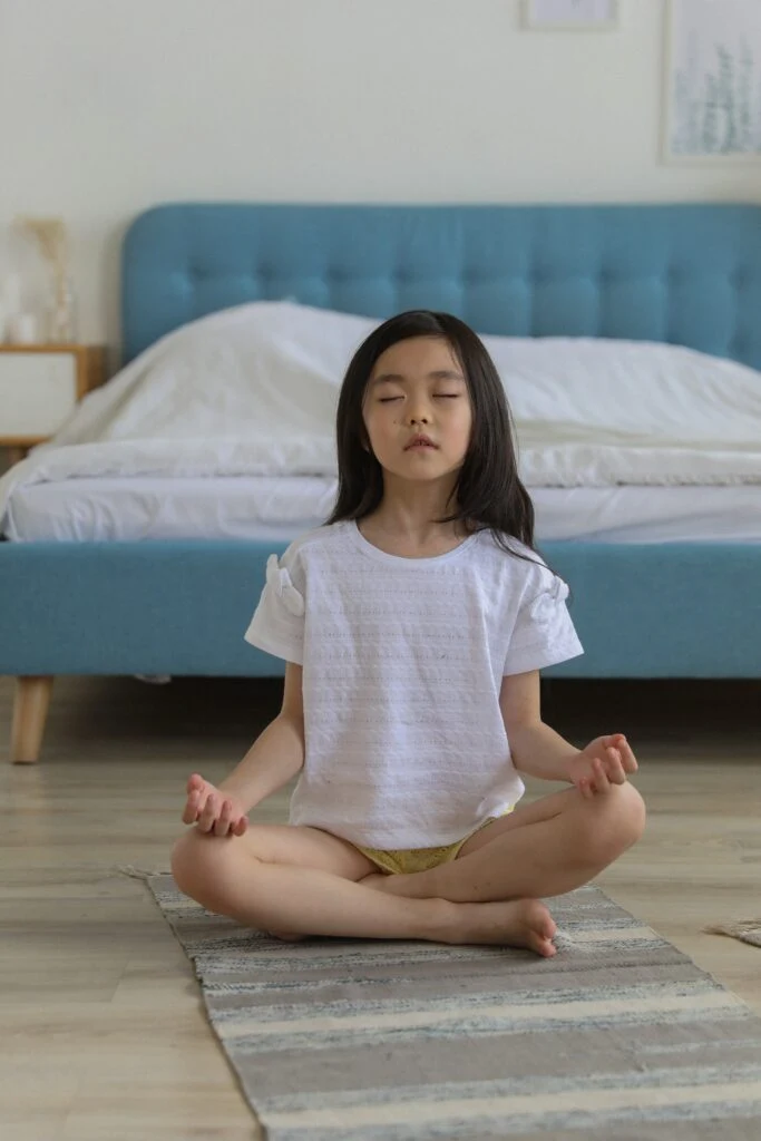 Girl sitting cross-legged and meditating in her bedroom
